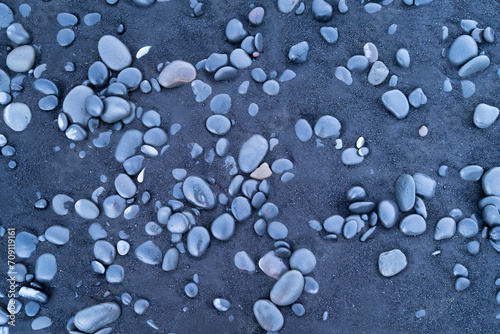 Black sand and pebble as a background. Round stones on the beach. Photography for design. Textures in nature.