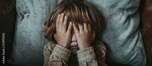 Child's pre-bedtime fear and night terrors; covering face in fear; child's experiences; view from above; sad psychological state. photo