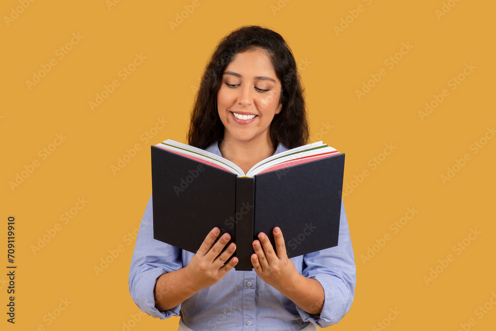 Content young woman with curly hair enjoying reading a book, showing a pleased smile