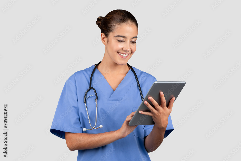 Engaged and friendly european nurse in blue scrubs focused on browsing a digital tablet Engaged and friendly european nurse in blue scrubs focused on browsing a digital tablet