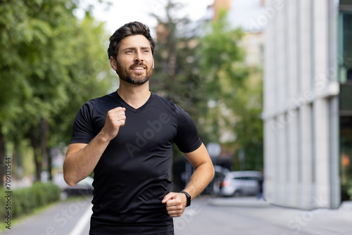 A young man in sportswear is running in the morning on a city street, smiling while looking to the side and feeling good. Close-up photo