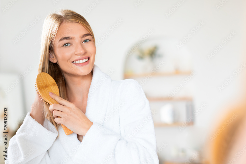 Young blonde woman smiling as she gently brushes hair indoor Young blonde woman smiling as she gently brushes hair indoor