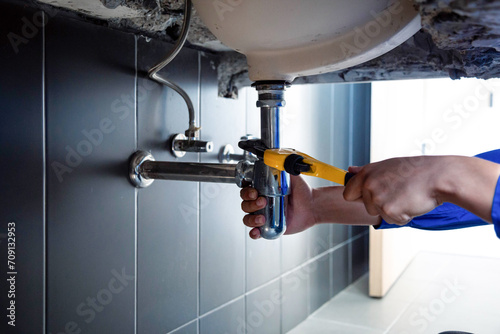 Plumber fixing white sink pipe with adjustable wrench.