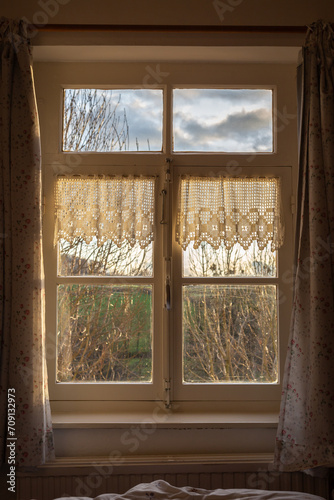 View of the natural countryside through an old-fashioned window with net curtains on the sides.