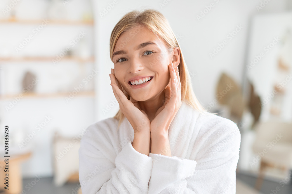 Blonde lady in bathrobe touches face showcasing glowing skin indoor Blonde lady in bathrobe touches face showcasing glowing skin indoor
