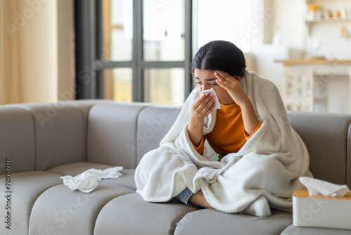 Indian woman feeling ill, sneezing into tissue at home