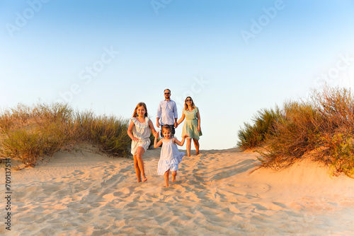 Happy family young parents two kids walking on sandy beach on sunny day during summer vacation