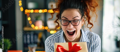 Excited female employee in office opening surprise gift box with happy expression. photo