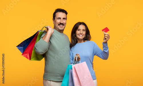 A joyful couple with a man holding colorful shopping bags and a woman holding a red credit card