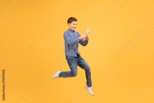 Happy Excited Teen Boy With Smartphone In Hands Jumping On Yellow Background