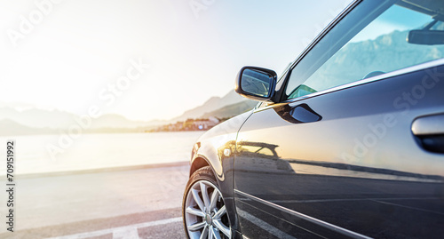 The car is parked on the embankment against the backdrop of the sea at sunset. photo