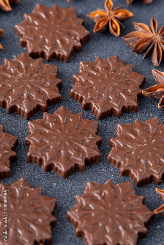 Chocolate candies in the shape of snowflakes. Brown food background.