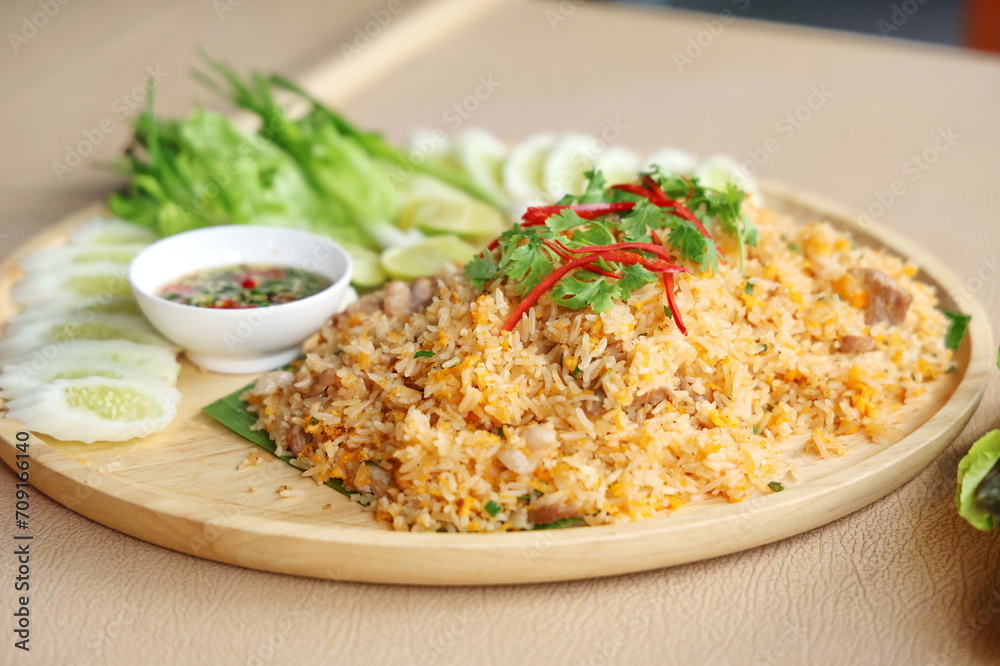 Pork fried rice with egg topped with coriander leaves and sliced red chili. Fried rice served on a wooden plate decorated with sliced cucumbers, lime wedges, spring onions and chili fish sauce.
Pork fried rice with egg topped with coriander leaves and sliced red chili. Fried rice served on a wooden plate decorated with sliced cucumbers, lime wedges, spring onions and chili fish sauce.