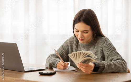 Obraz na plátně Happy young woman budgeting with cash and calculator at desk