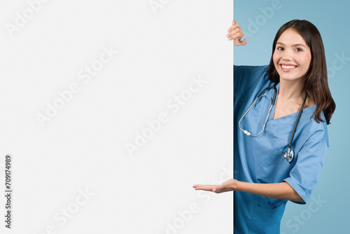 Young nurse in blue, pointing at empty board, blue backdrop photo