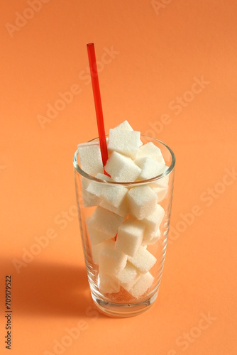 On an orange background there is a glass glass with refined sugar with a straw.