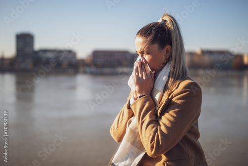 Woman blowing nose while sitting by the river on a sunny winter day.	Toned image. photo