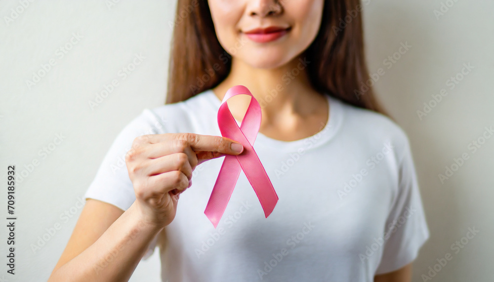 Woman's hand holds pink ribbon, symbolizing breast cancer awareness and medical care Woman's hand holds pink ribbon, symbolizing breast cancer awareness and medical care
