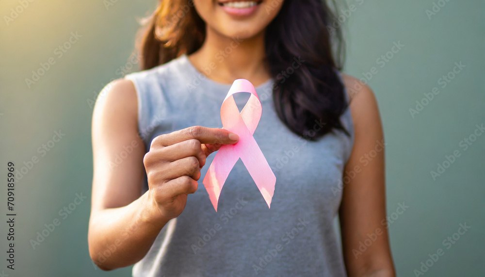 Woman's hand holds pink ribbon, symbolizing breast cancer awareness and medical care Woman's hand holds pink ribbon, symbolizing breast cancer awareness and medical care