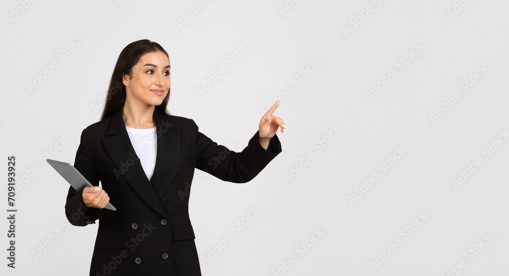 Young caucasian businesswoman in suit with tablet, pointing finger at copy space, use virtual screen, gray background Young caucasian businesswoman in suit with tablet, pointing finger at copy space, use virtual screen, gray background