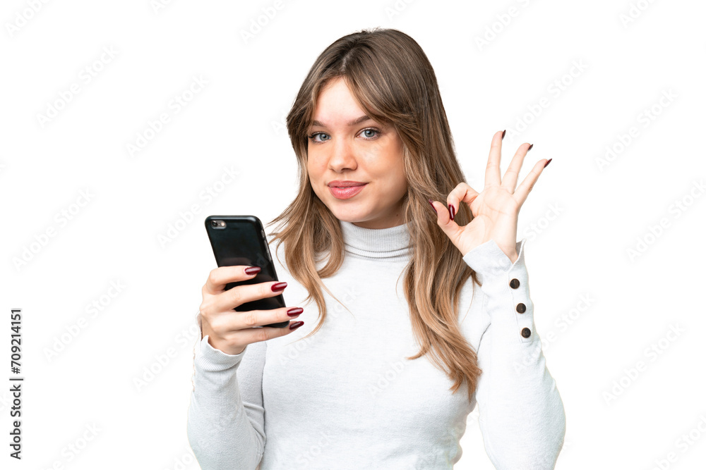 Young girl over isolated chroma key background using mobile phone and doing OK sign Young girl over isolated chroma key background using mobile phone and doing OK sign