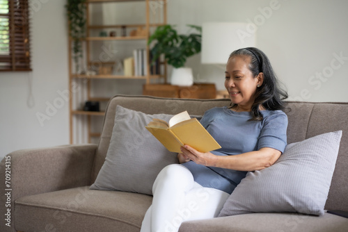 Senior asian old woman sitting on sofa in the living room reading a book to relax on a leisure day.