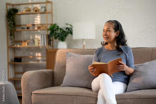 Senior asian old woman sitting on sofa in the living room reading a book to relax on a leisure day.