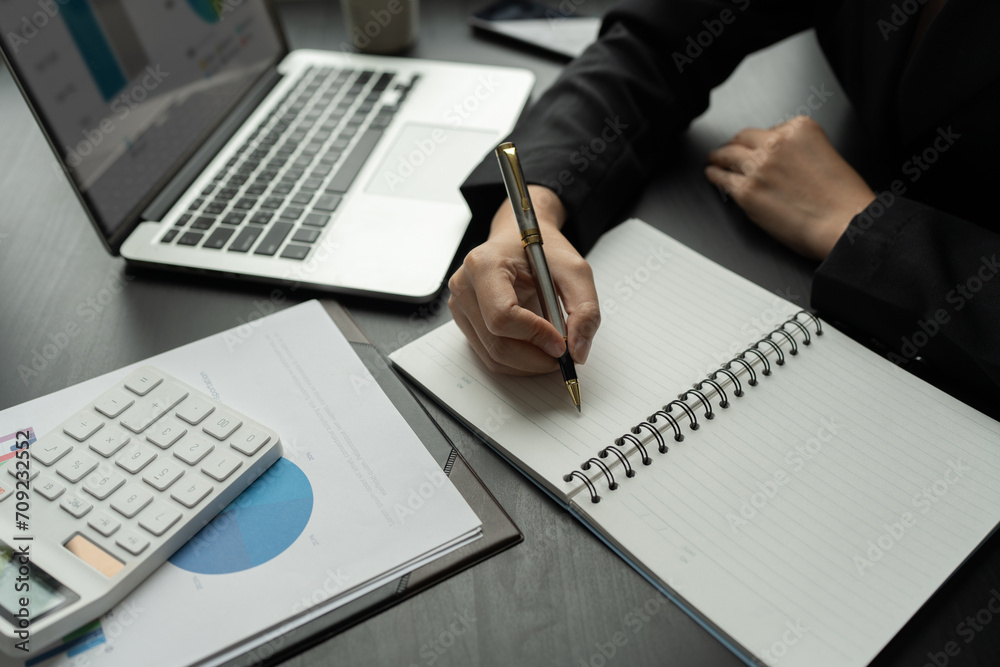Asian business woman Calculate report with calculator. Take note. Have notepad to remember to do financial report or profit.