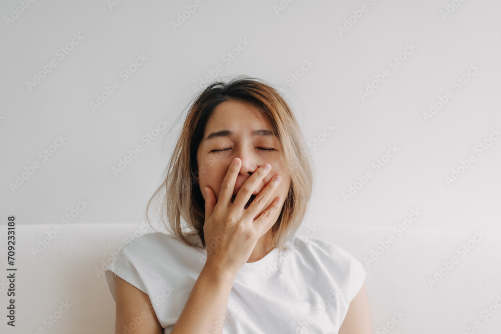 Sleepy face Asian woman yawning and rubbing her eyes in white t-shirt sits on the sofa. Sleepy face Asian woman yawning and rubbing her eyes in white t-shirt sits on the sofa.