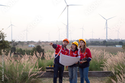 Group of maintenance engineers preparing and planning inspection of wind turbines, holding tablets, looking at wind turbines