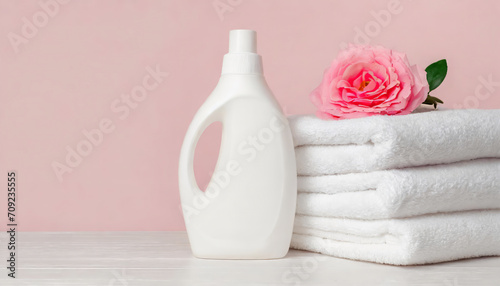 Plastic liquid detergent bottle and white towels. Fabric softener. Regular washing, laundry concept on pink background with copy space photo