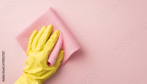 Top view of hand in yellow glove holding pastel pink rag on pink background with copy space