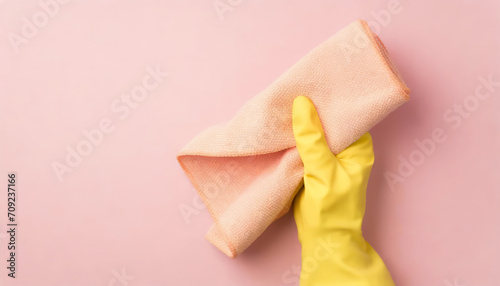 Top view of hand in yellow glove holding pastel pink rag on pink background with copy space photo