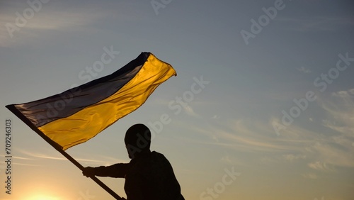 Young man in military uniform waving flag of Ukraine against beautiful sunset at background. Male ukrainian army soldier lifted national banner at countryside. Victory against aggression photo