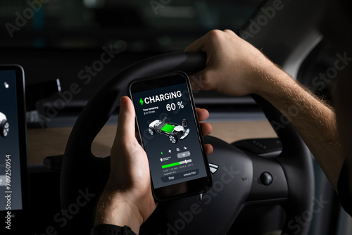 Electric car driver checks battery charging status, range and charging limit on app screen in the car. Smart technology device show EV car recharging data of electric storage in car battery innards.