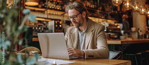 Man happily typing on laptop for work in a coffee shop, researching and writing for freelance blog and customer insights, as well as browsing the internet in restaurant.