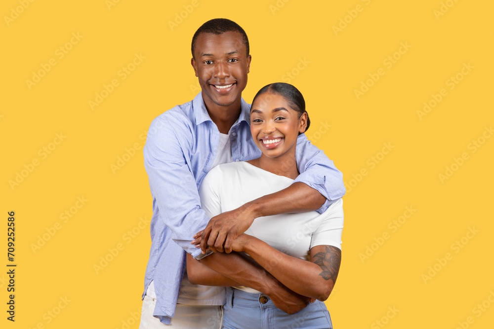 Smiling black couple hugging, looking at camera on yellow background Smiling black couple hugging, looking at camera on yellow background