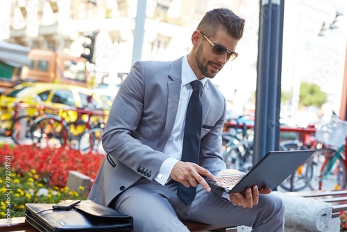Businessman sitting on brench working with laptop on street. photo