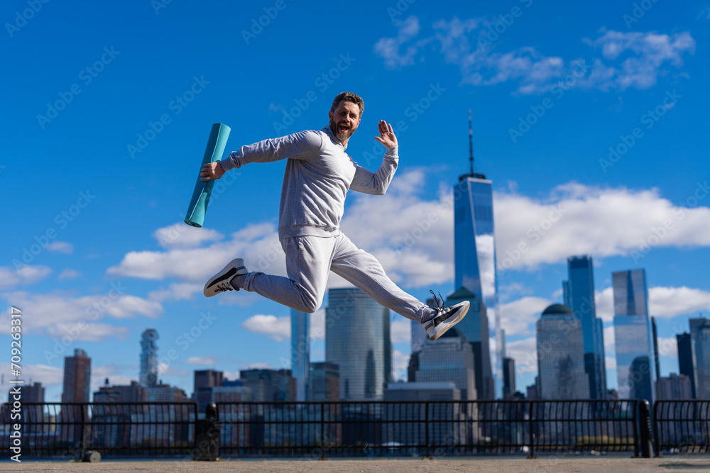Man jumping with energy. Sport lifestyle. Sportsman running with fitness mat. Sport man training outdoor in New York. Healthy lifestyle with daily fitness. Fitness and sport. Fitness routine