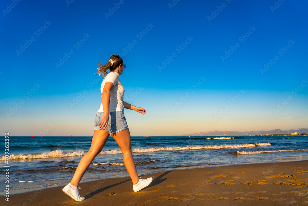 Beach holiday - beautiful woman walking, running on sunny beach - Costa Dorada Spain 
