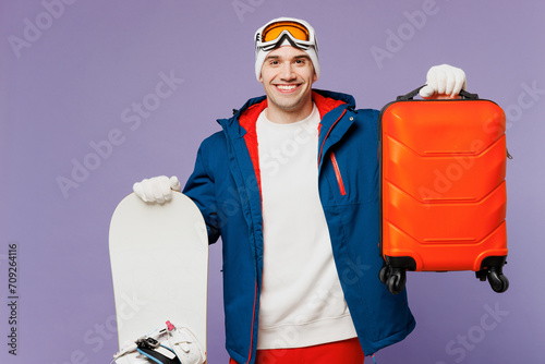 Traveler fun happy man wear blue windbreaker jacket ski goggles mask hold snowboard bag look aside isolated on plain purple background. Tourist travel abroad in free time getaway. Air flight concept. #709264116