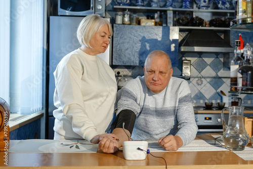 An elderly woman measures her husband's blood pressure and pulse.