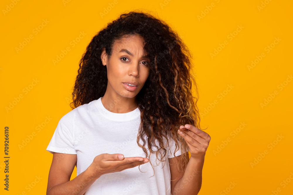 Displeased black lady showing her dry damaged hair ends, studio