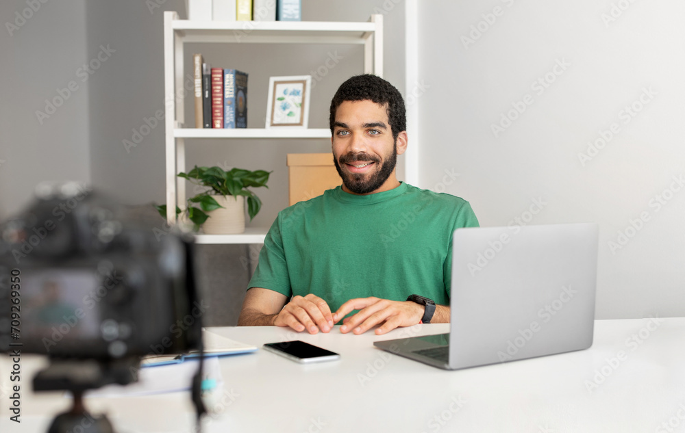 Smiling man in a green shirt sitting at a desk with a laptop, smartwatch Smiling man in a green shirt sitting at a desk with a laptop, smartwatch