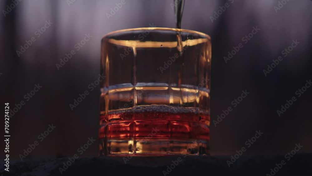 Glass of whiskey being poured in the outdoors in front of a large fire