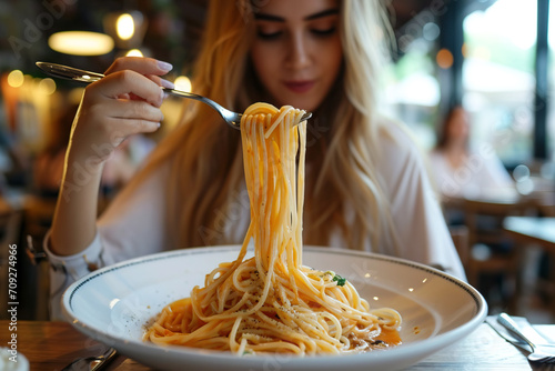 A woman in a restaurant holds up her spaghetti with a spoon fork while inspecting it closely