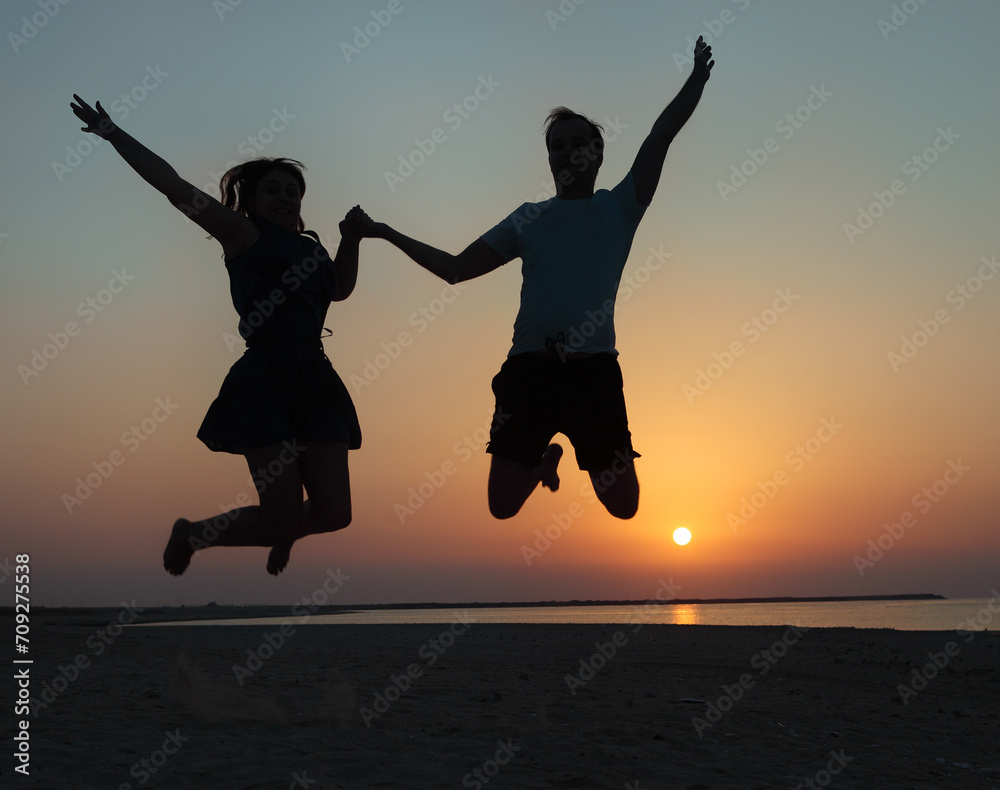Silhouette of a couple - man and woman jumping on the beach
