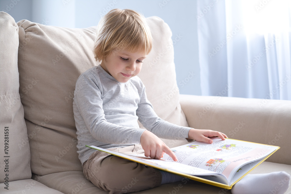 little boy reading book, sitting on sofa at home little boy reading book, sitting on sofa at home