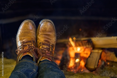 Man resting at fireplace, warming his feet and drying boots. Cozy warm of the home in cold winter.