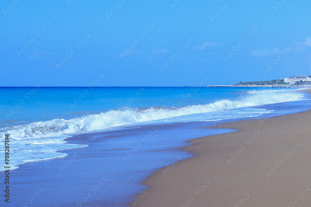 Sandy beach sea shore with blue wave and white foam. Sea ​​waves on the sand on the beach. Blue sea waves on the beach for background. Beach sand and soft wave background. Vacation travel holiday 